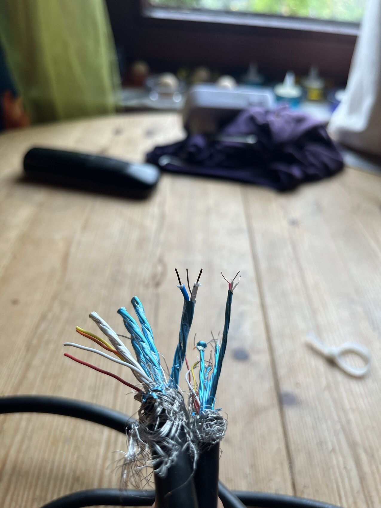 Aufgeschnittene Netzwerkkabel mit bunten Adern auf Holztisch, unscharfer Hintergrund.