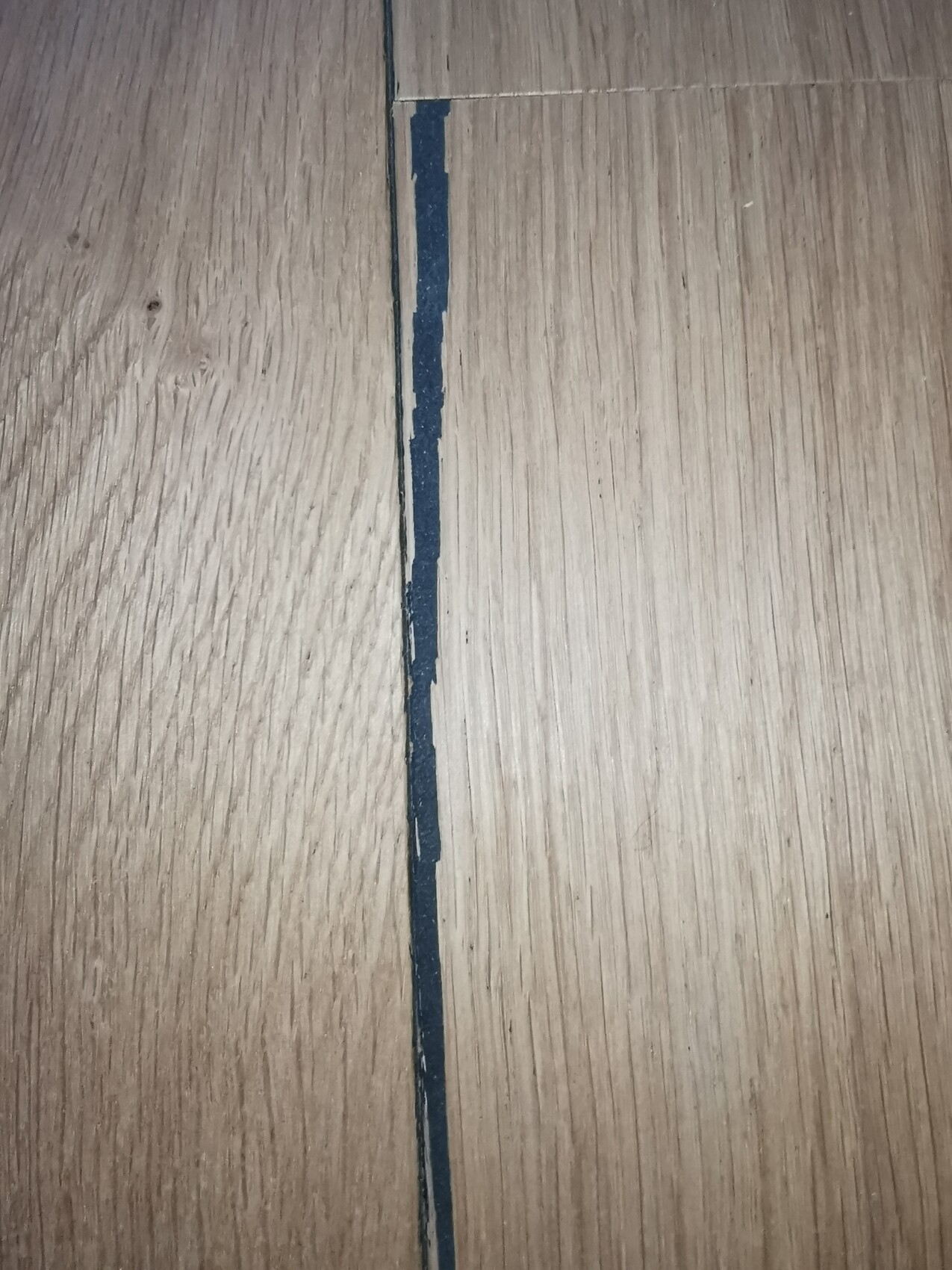 Holzdielenboden mit einer engen blauen Linie entlang der Fuge zwischen zwei Dielen.
