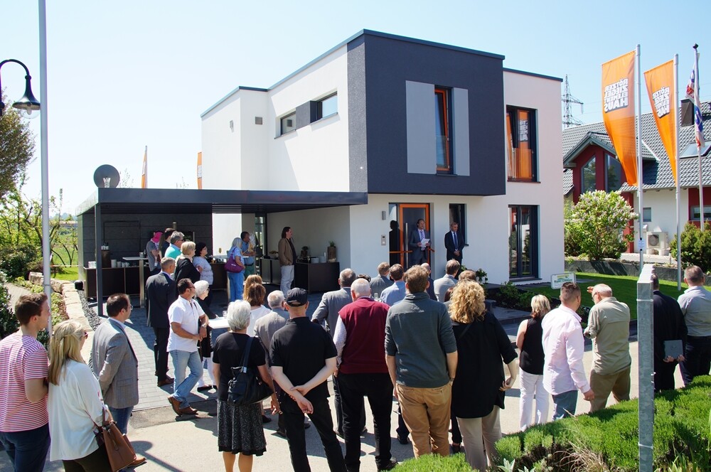 Moderne zweigeschossige Villa mit Feier; viele Menschen vor dem Eingang.