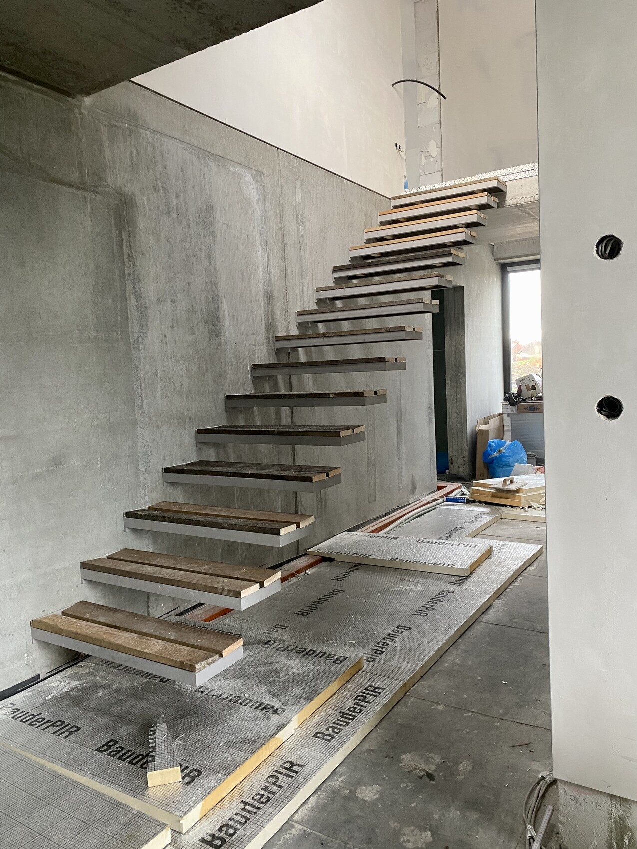 Schwebende Holzstufen einer Treppe an einer rohen Betonwand auf einer Innenbaustelle