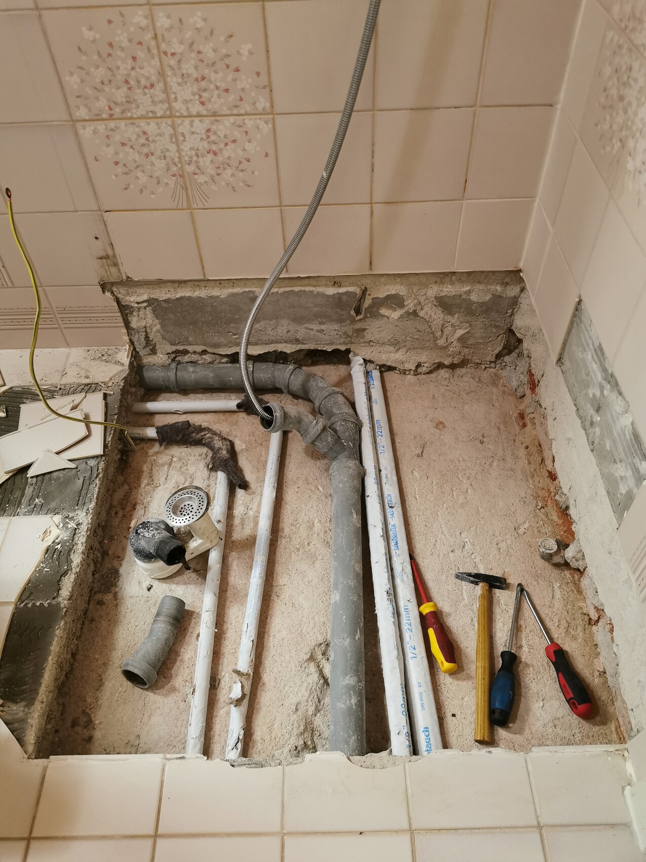 Freigelegter Badezimmerboden mit Rohren, Abfluss, Fliesenresten und Werkzeugen.