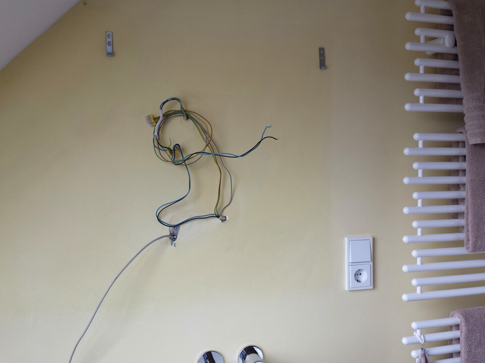 Offene Kabel an der Wand neben Heizkörper und Steckdose im Innenraum.