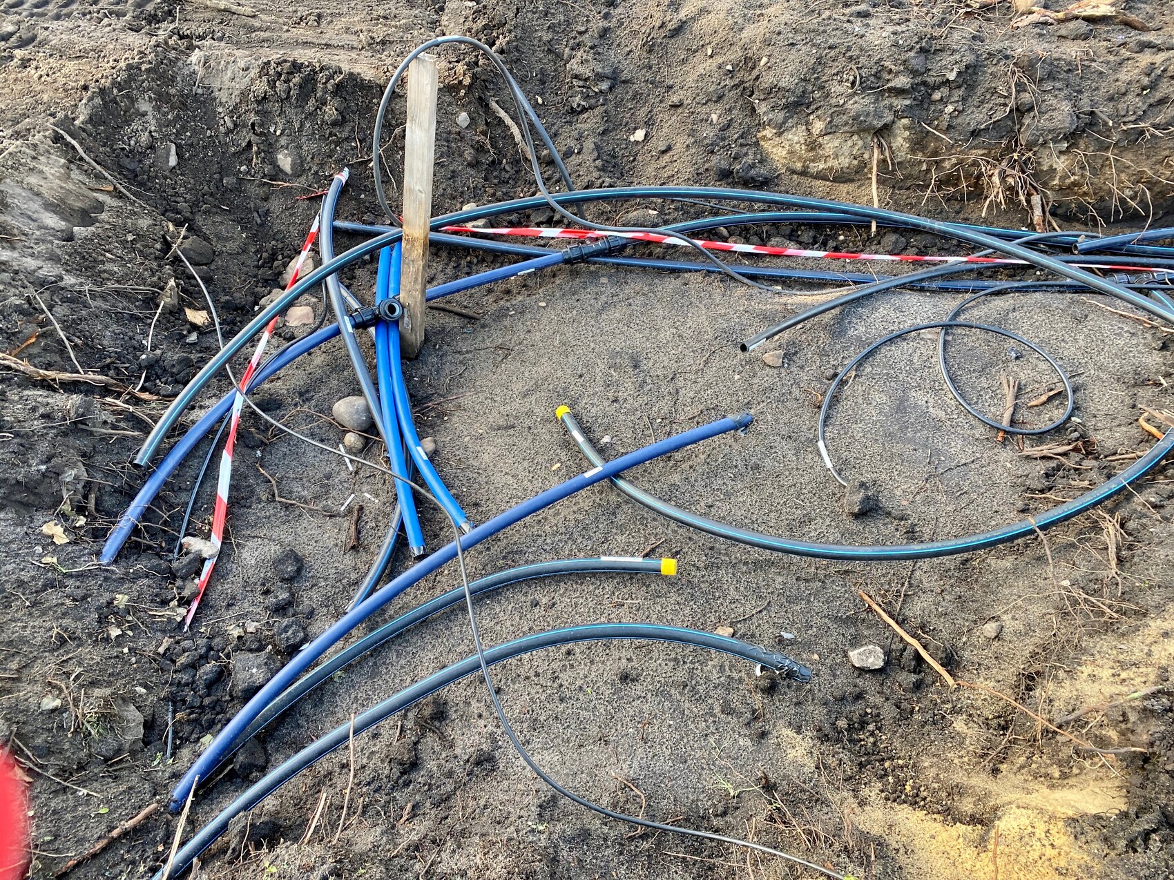 Ausgrabung mit lose verlegten Kabeln und Schläuchen; blaue und schwarze Leitungen.