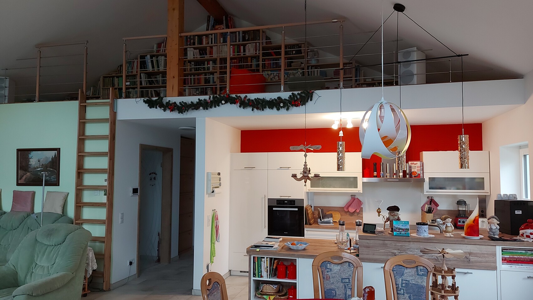 Offene Küche mit rotem Wandpanel, Insel, Hängeleuchten; Mezzanin mit Bücherregal.