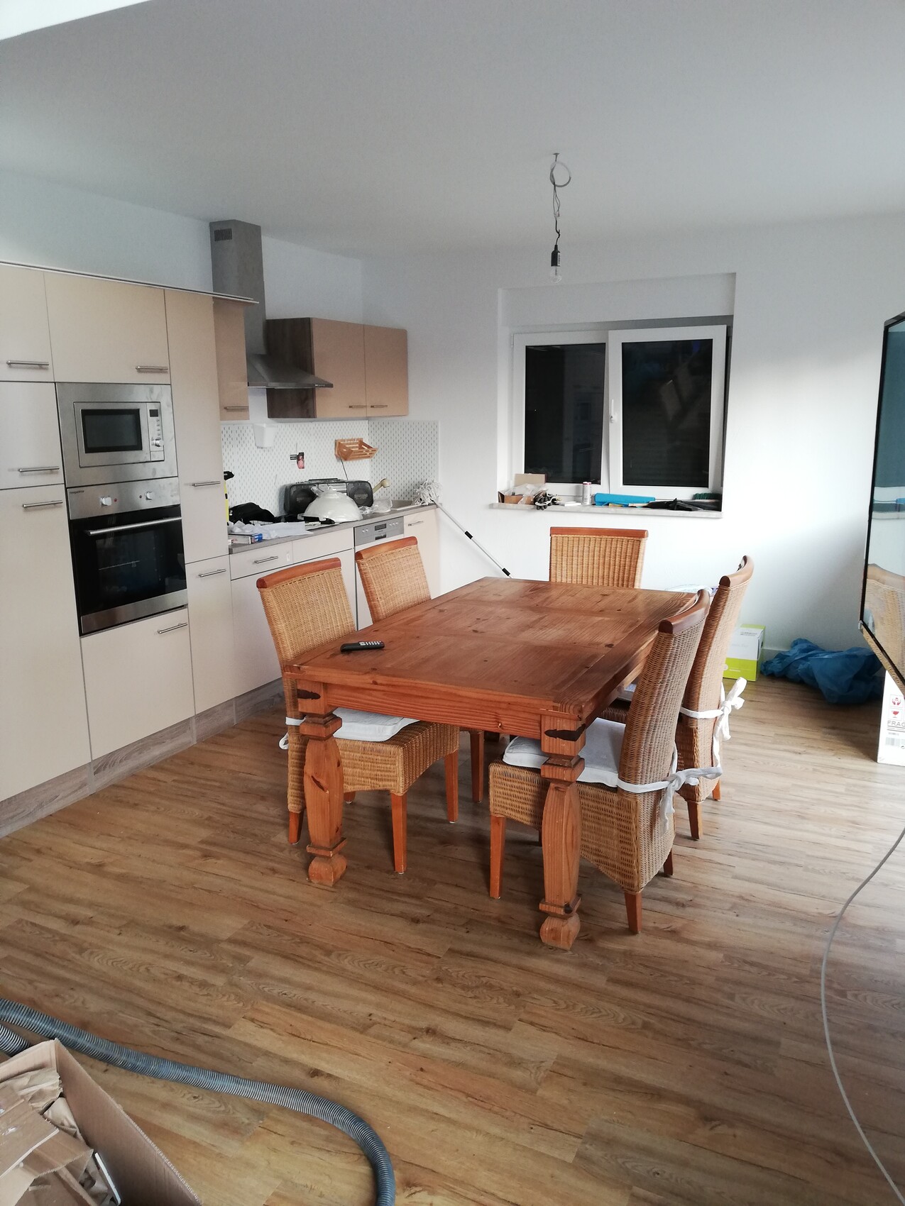 Küche mit Holztisch und Korbstühle, linke Küchenzeile, offene Glühbirne an Kabeln von der Decke