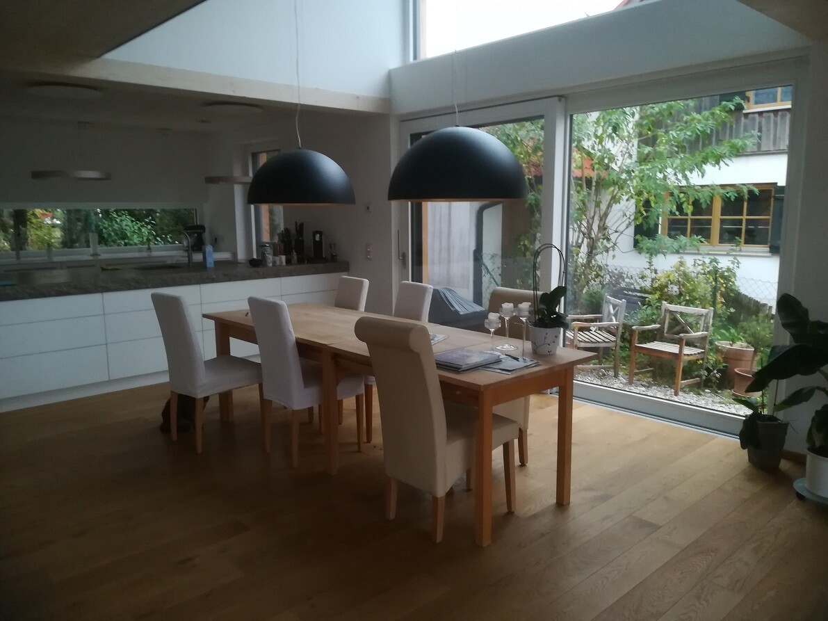 Offener Essbereich mit Holztisch, beigen Stühlen, schwarzen Pendelleuchten und Gartenblick.