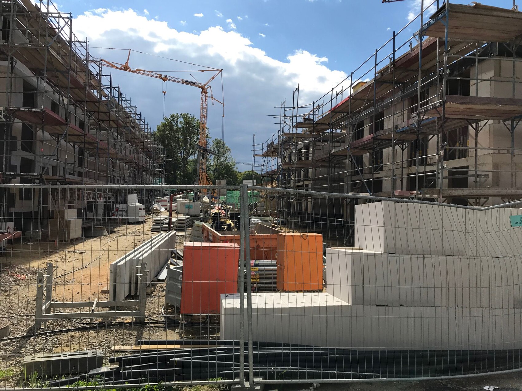 Baustelle: Gerüste an zwei Gebäuden, Kran im Hintergrund, Bauzubehör und Zaun.