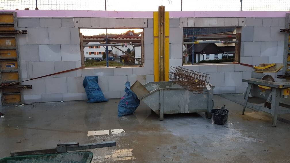 Baustelle im Rohbau: Betonblockwände, blaue Säcke, Metallbehälter mit Bewehrung, Säge.