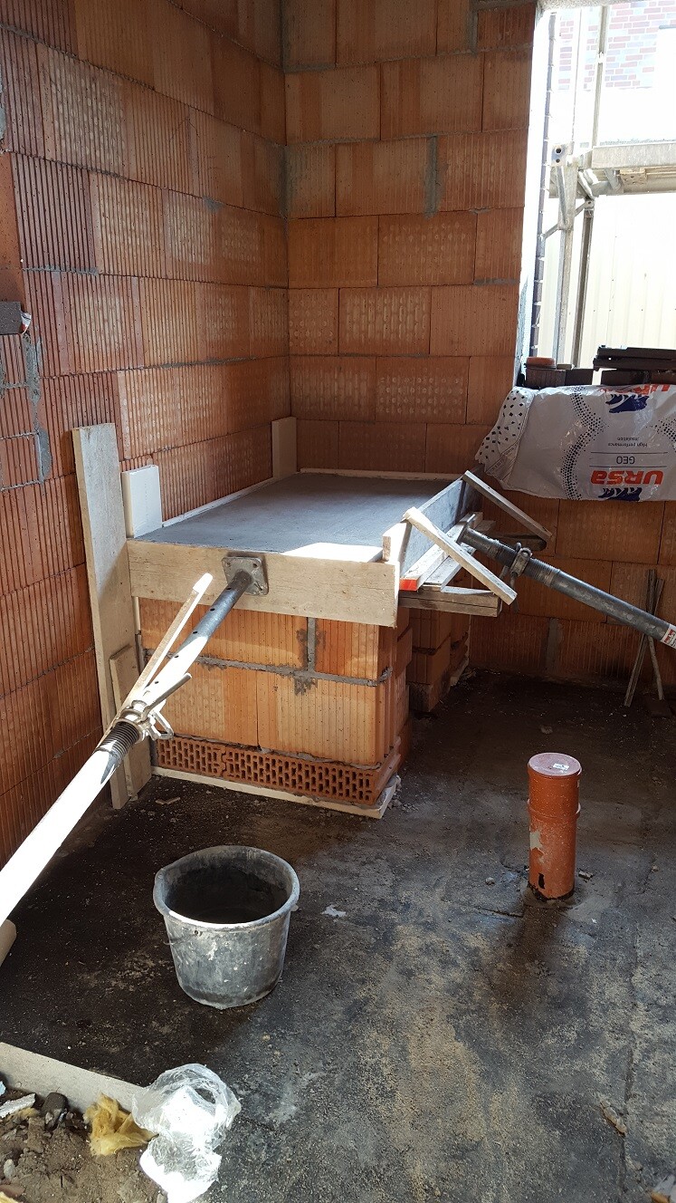Baustelle: rohes Backsteinmauerwerk, provisorische Betonplatte mit Holzform, Eimer und Rohre.