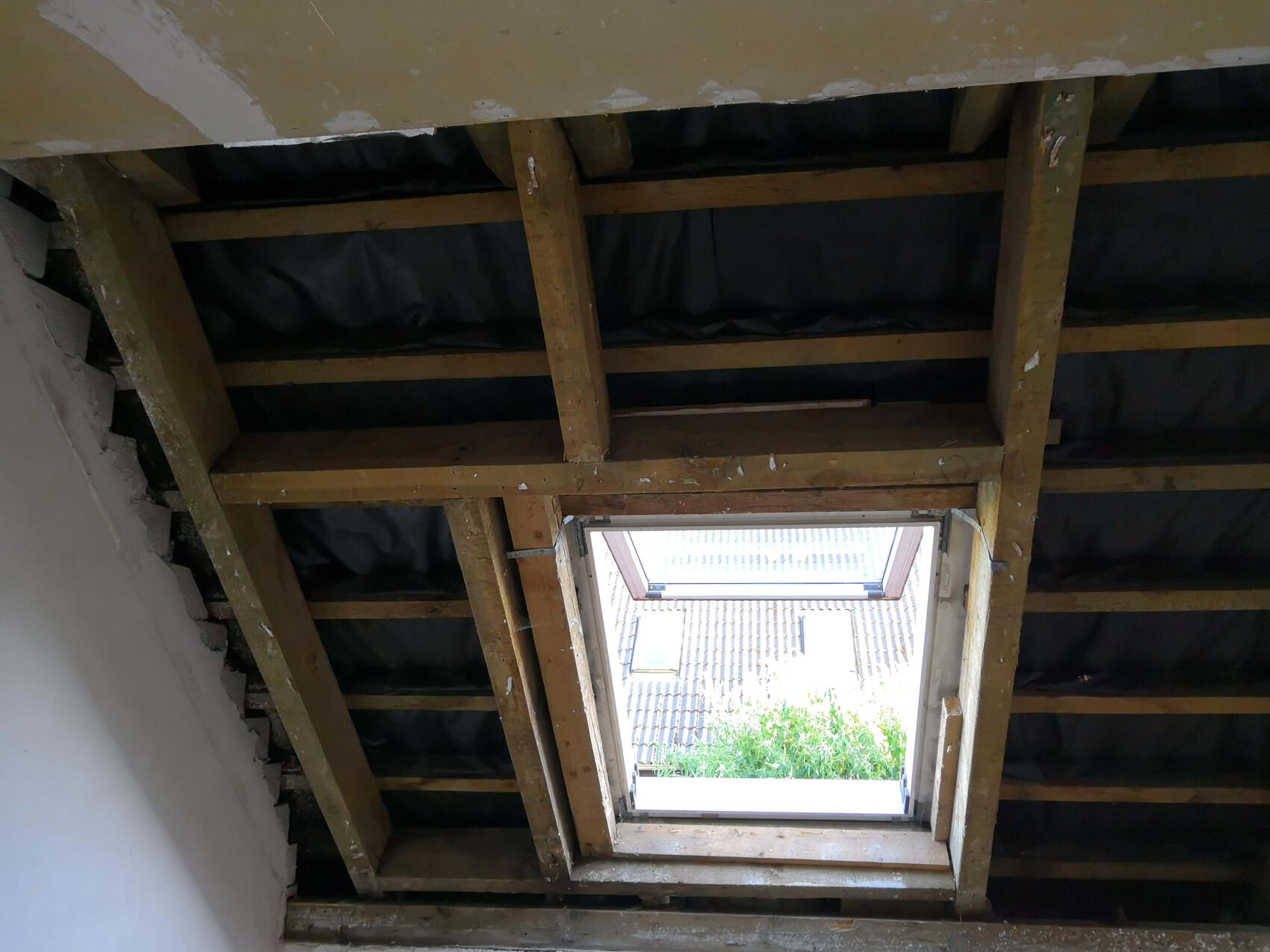 Dachboden mit Holzbalken, dunkler Dämmung, offenes Dachfenster mit Blick nach außen.