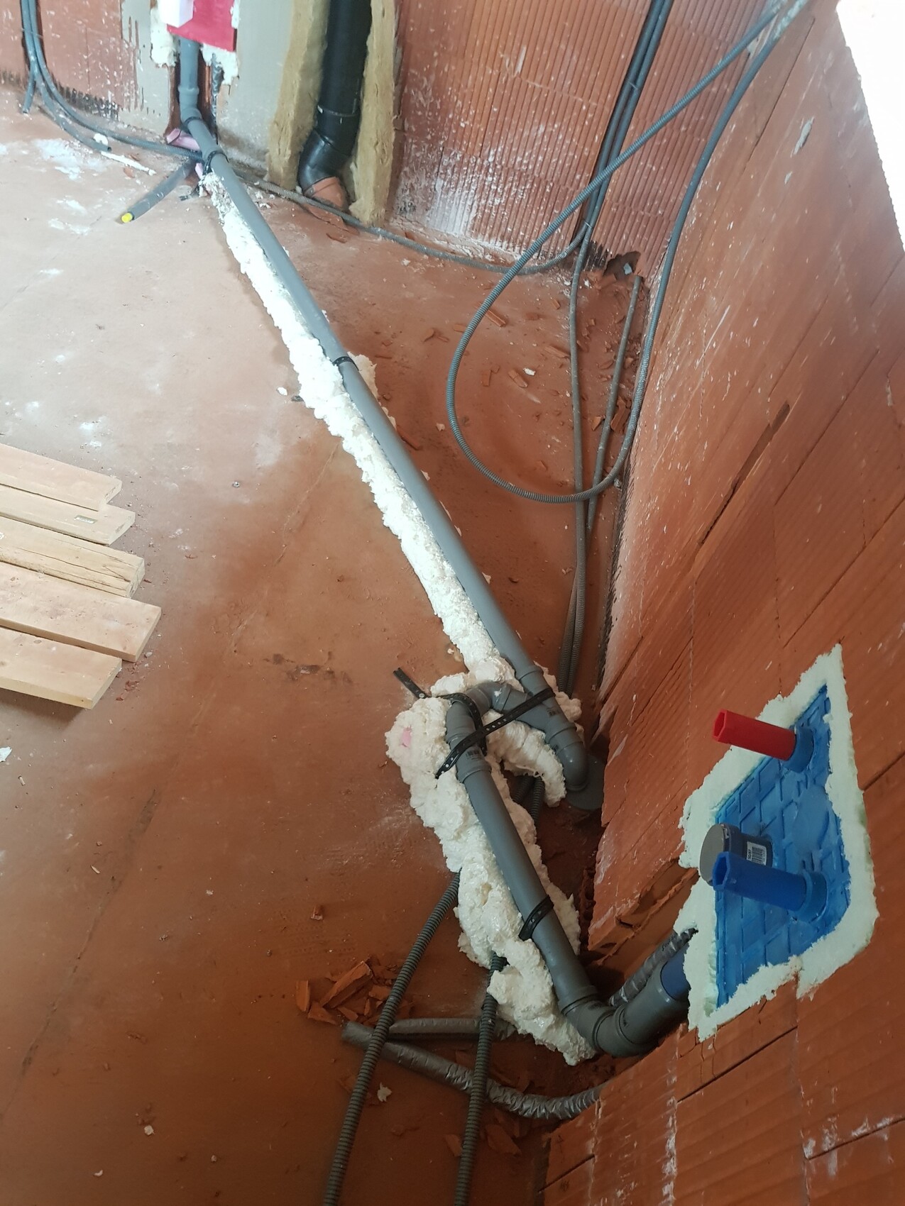 Kellerbaustelle: Mehrere graue PVC-Rohre, Schaumisolierung um Rohre, offener Wanddurchbruch.