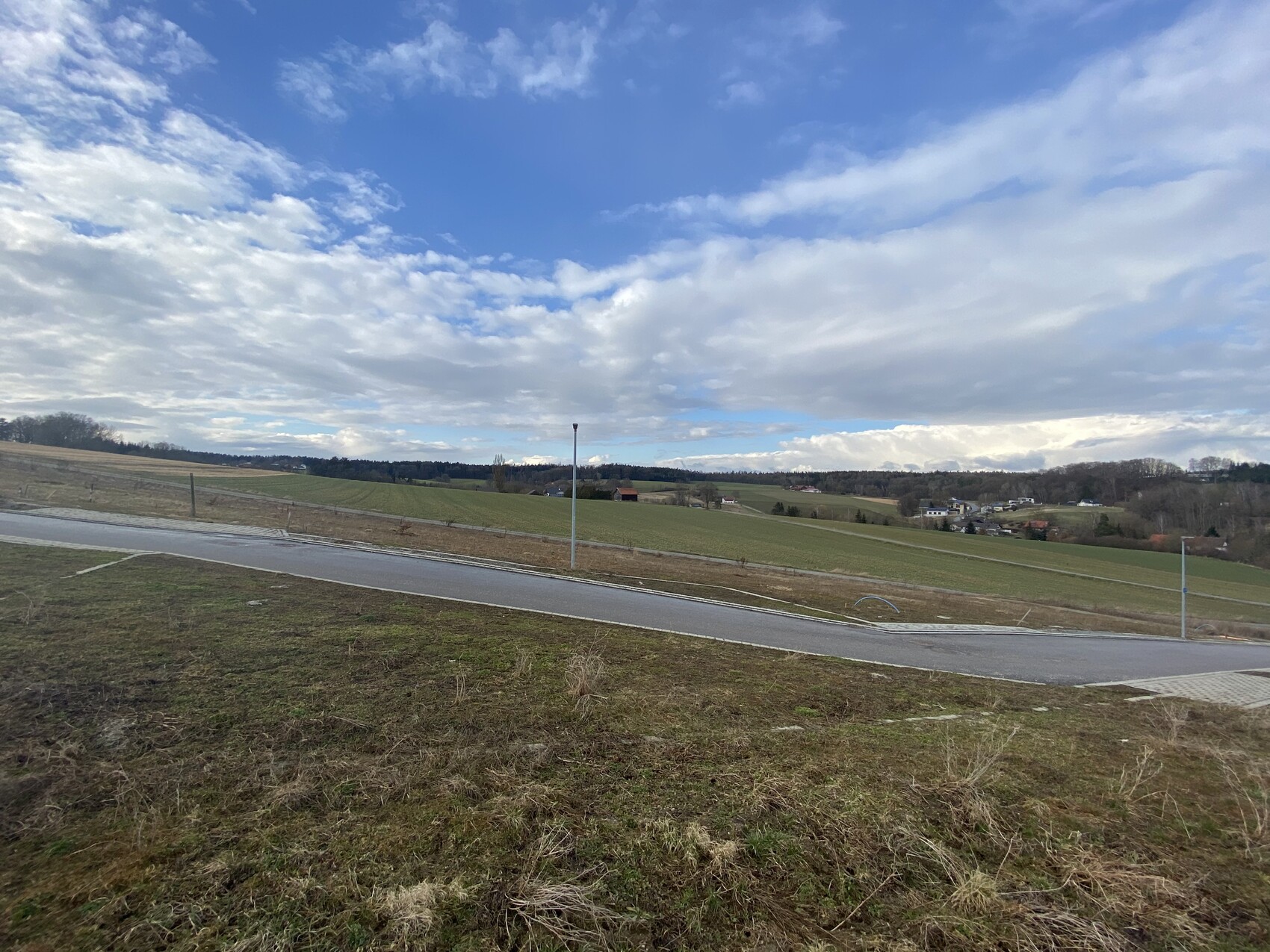 Landschaft mit Feldern, Straße und Häusern am Horizont unter blauem Himmel.