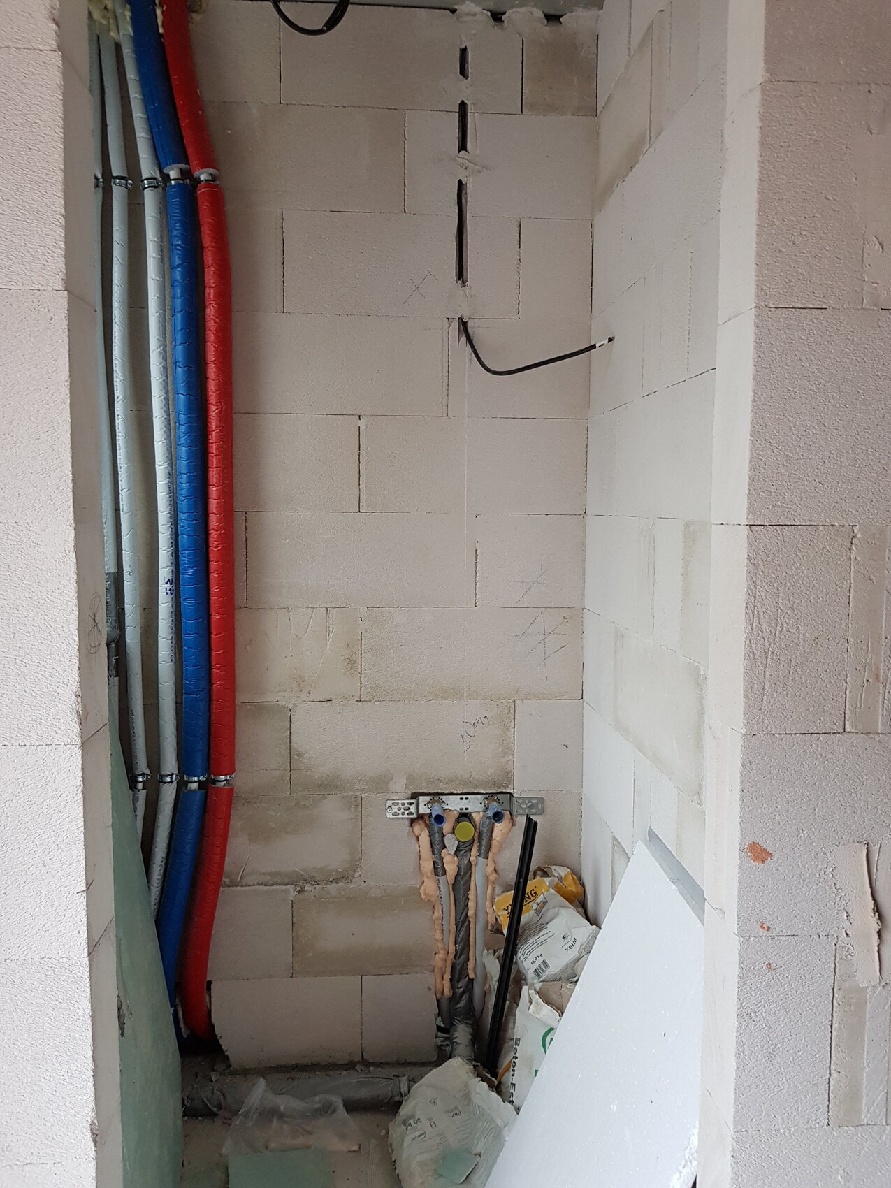 Installationsraum mit farbigen Wasserleitungen (rot/blau) an der Wand.