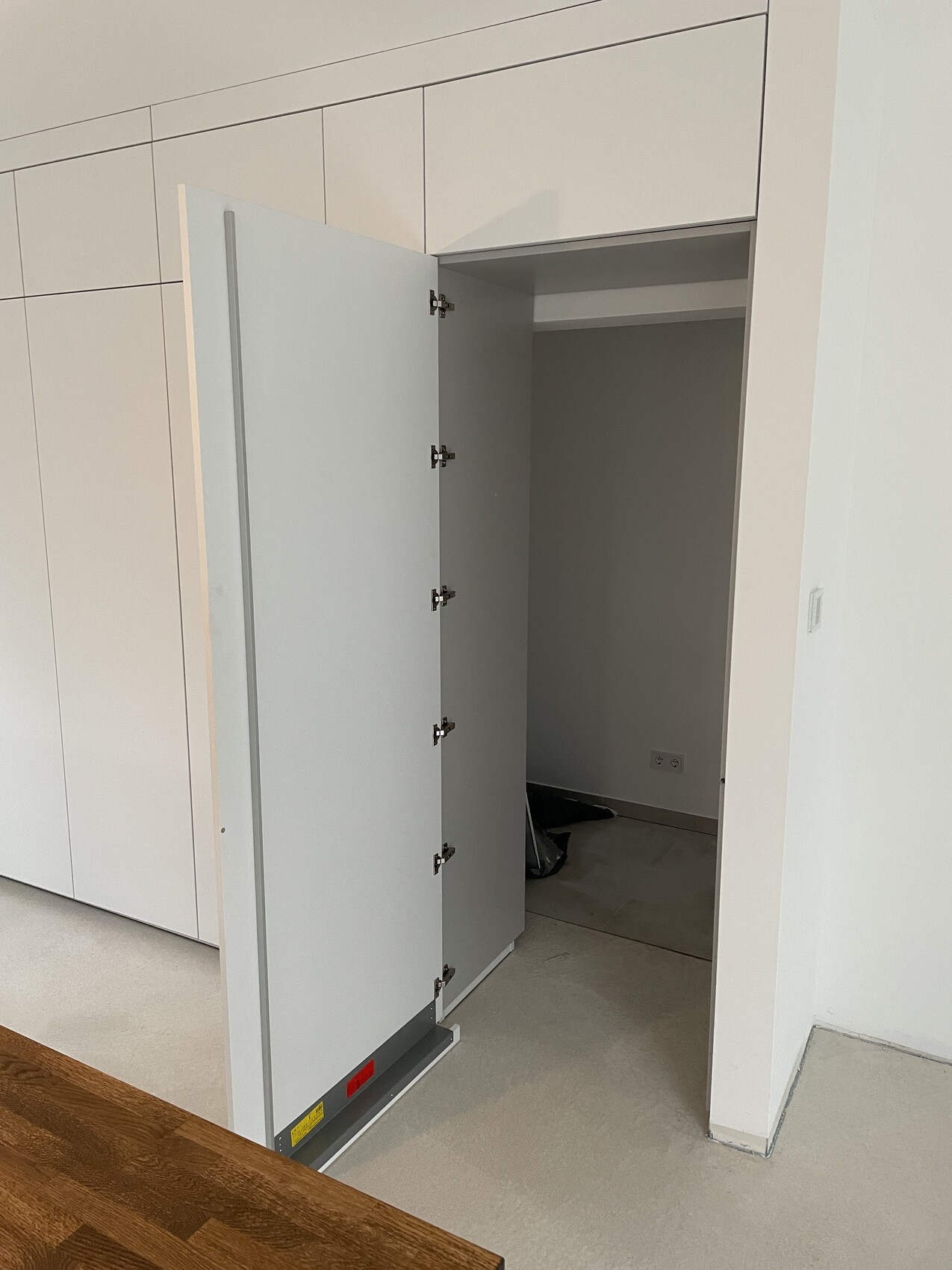 Offene weiße Einbauschranktür im modernen Innenraum, graue Innenseite, Holztisch im Vordergrund