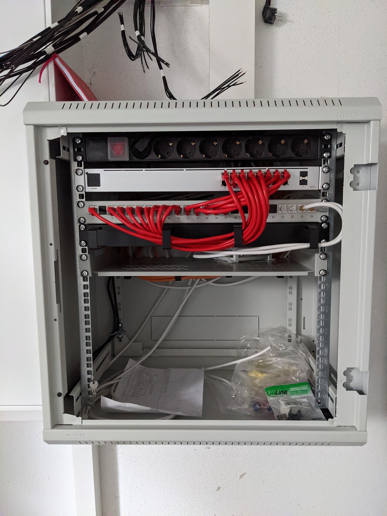 Offenes Schaltschrank-Gehäuse mit vielen roten Patchkabeln, Patchpanel und Notizen.