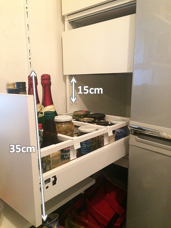 Offener Küchen-Auszugsschrank mit Vorratsbehältern, Flaschen und Kühlschrank daneben.