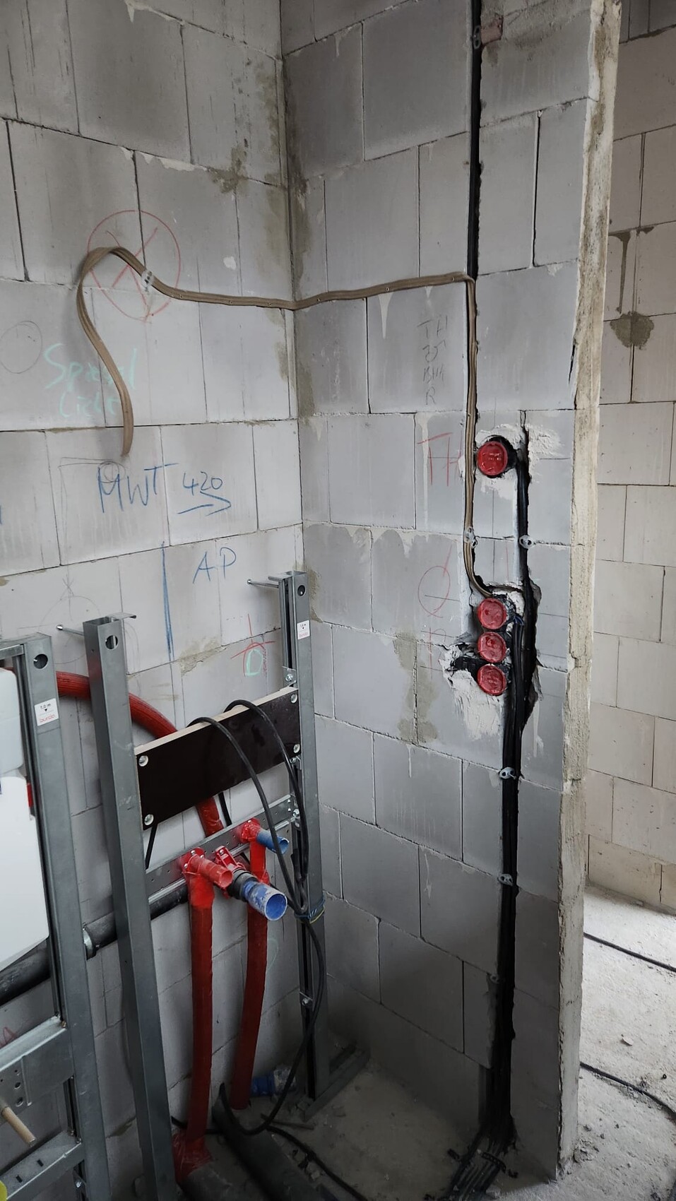 Rohbau-Raum: graue Betonwand, rotes PEX-Rohr, schwarze Kabel, Metallrahmen und Installationen.