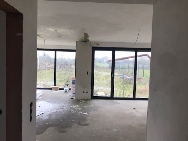 Neubau-Wohnraum im Rohbau mit großen Glas-Türen und offenen Fenstern.