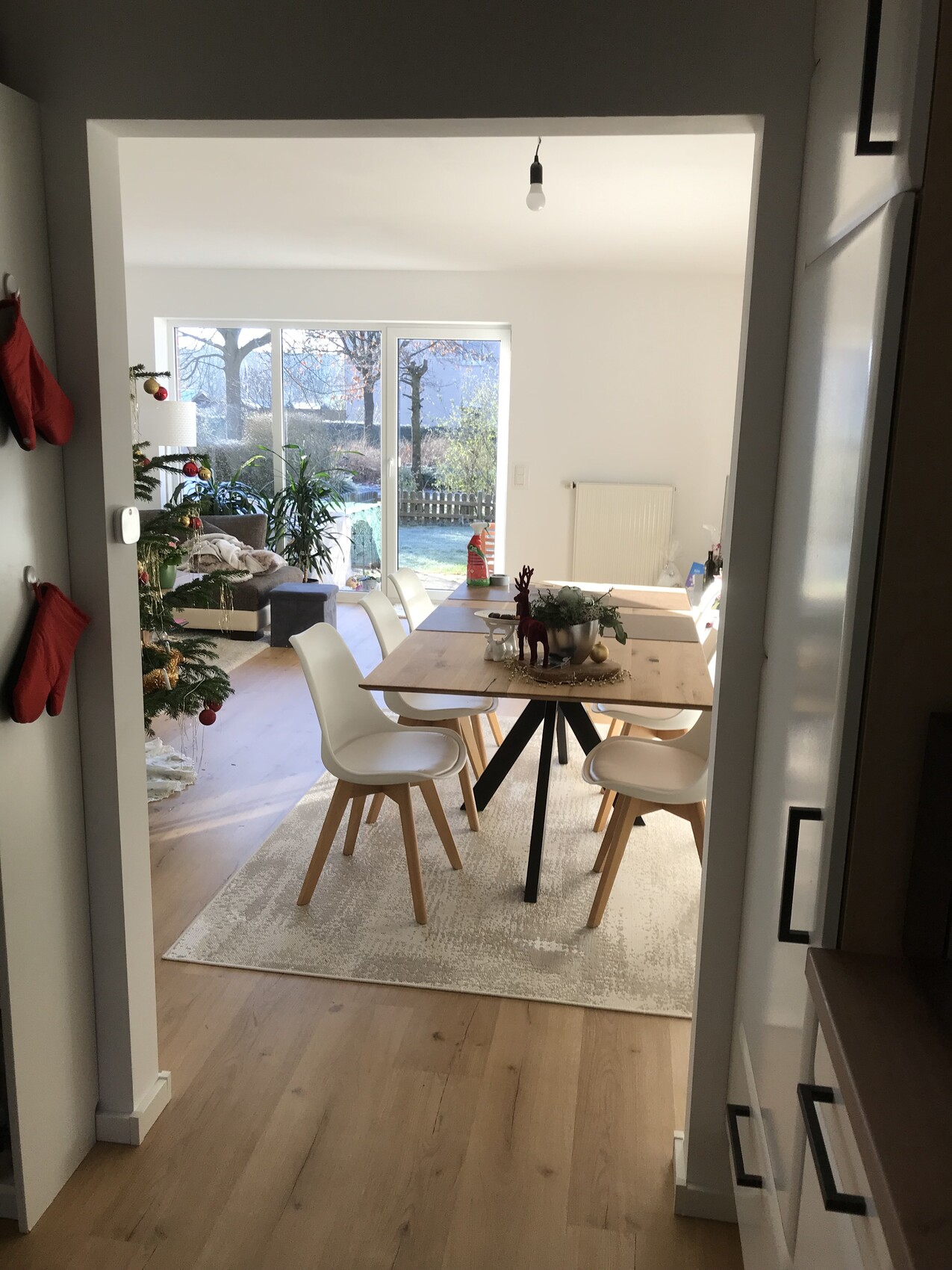 Heller Essbereich mit Holztisch, weißen Stühlen, Weihnachtsbaum und Glas-Schiebetür zum Garten.