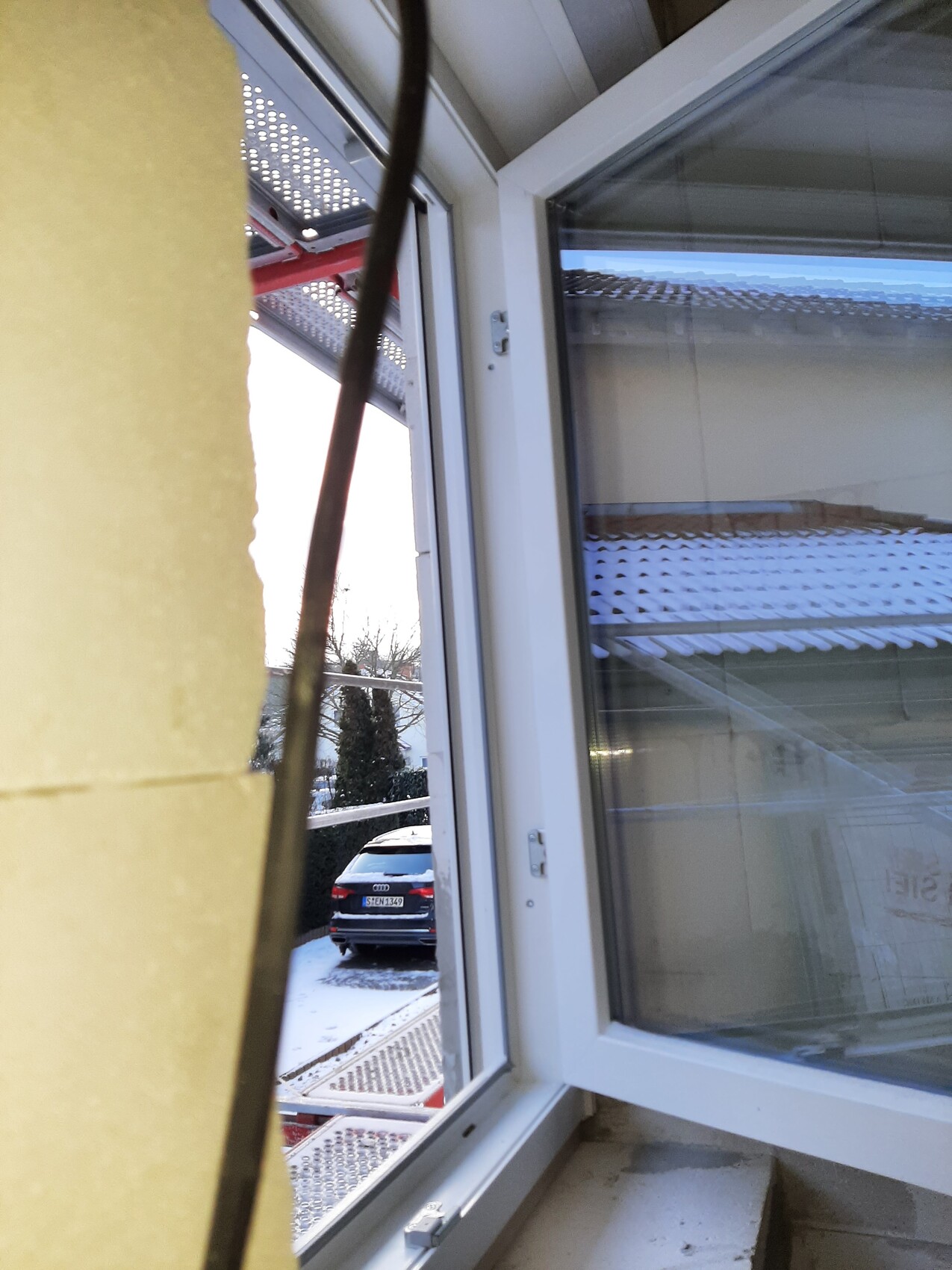 Offenes Fenster mit gelbem Pfeiler links; Blick auf schneebedeckten Parkplatz mit Auto.