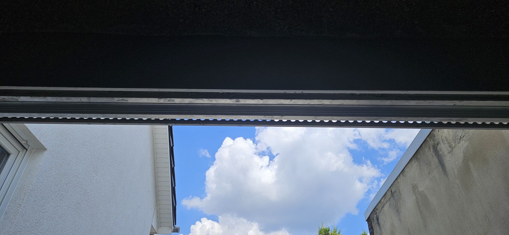 Blick von innen durch eine Öffnung auf blauen Himmel mit Wolken; seitliche weiße und graue Wände