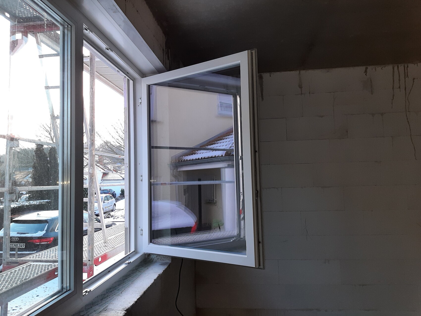 Offenes Fenster in renoviertem Innenraum, Blick nach draußen auf Baugerüst und verschneite Autos.