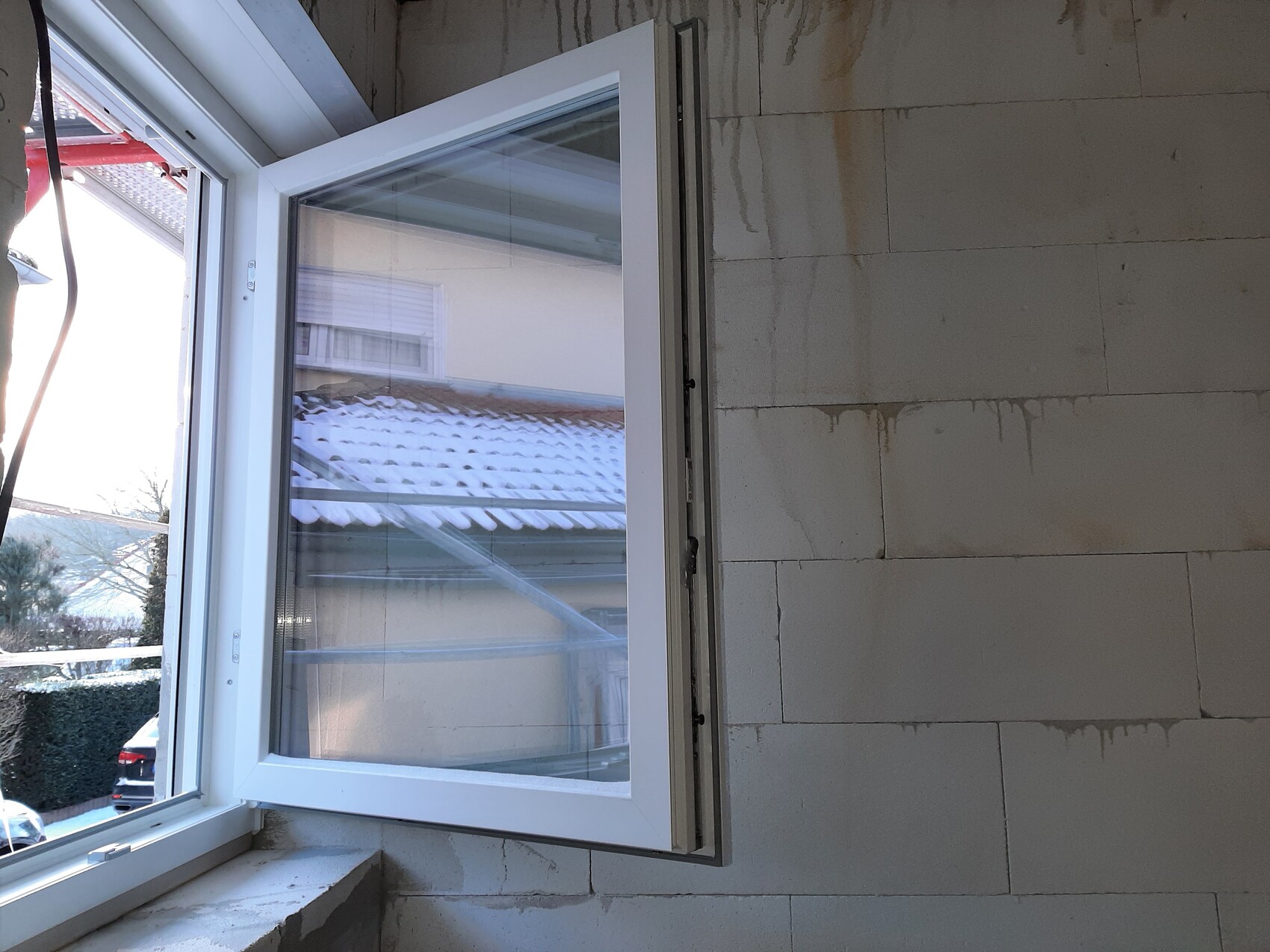 Offenes Fenster in einem unfertigen Innenraum mit Betonwänden; Blick auf verschneites Dach draußen.