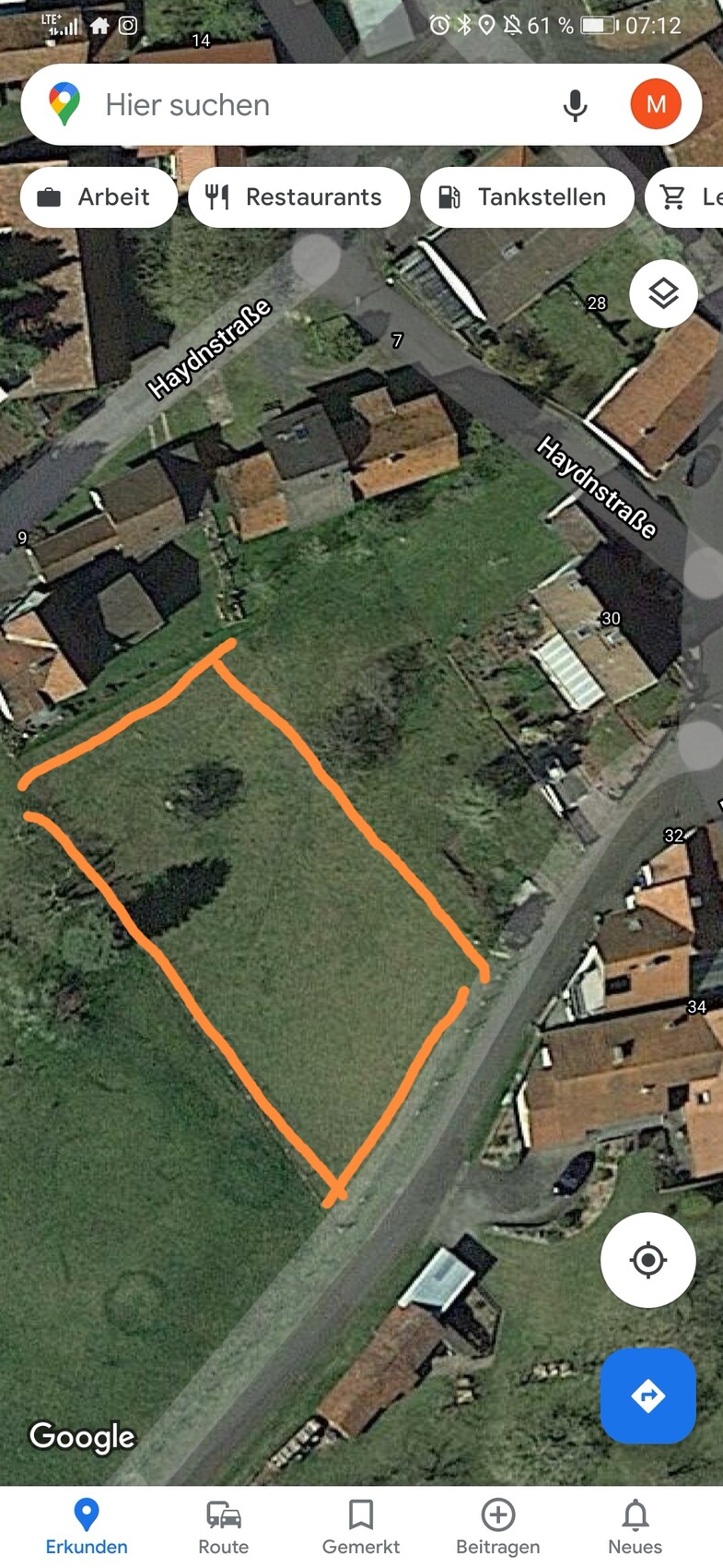 Satellitenbild eines grünen rechteckigen Grundstücks mit orange Umrandung neben einer Straße.