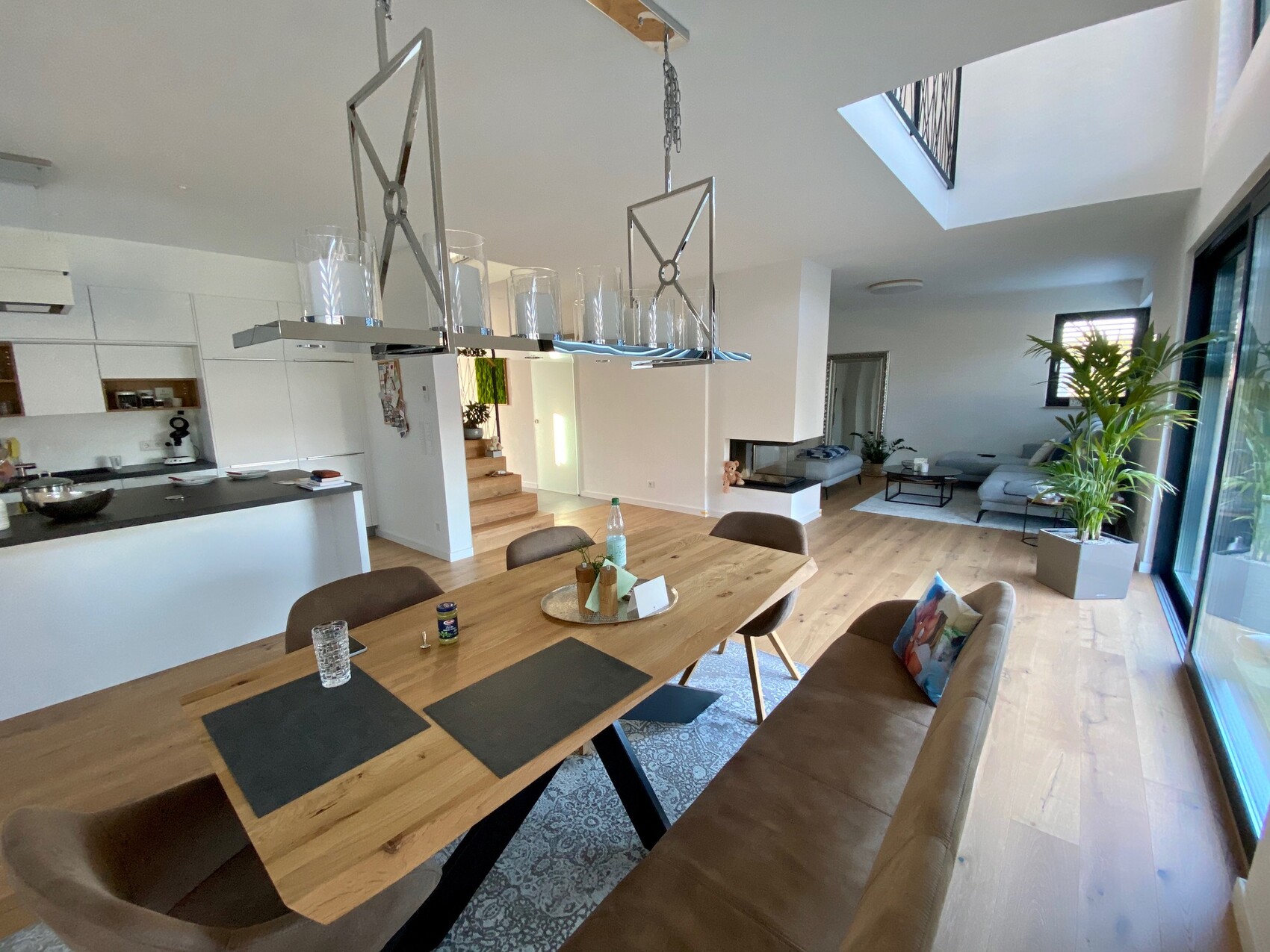 Offener Wohn- und Essbereich: Holztisch, Stühle, Küche links, Sofa und Pflanze.