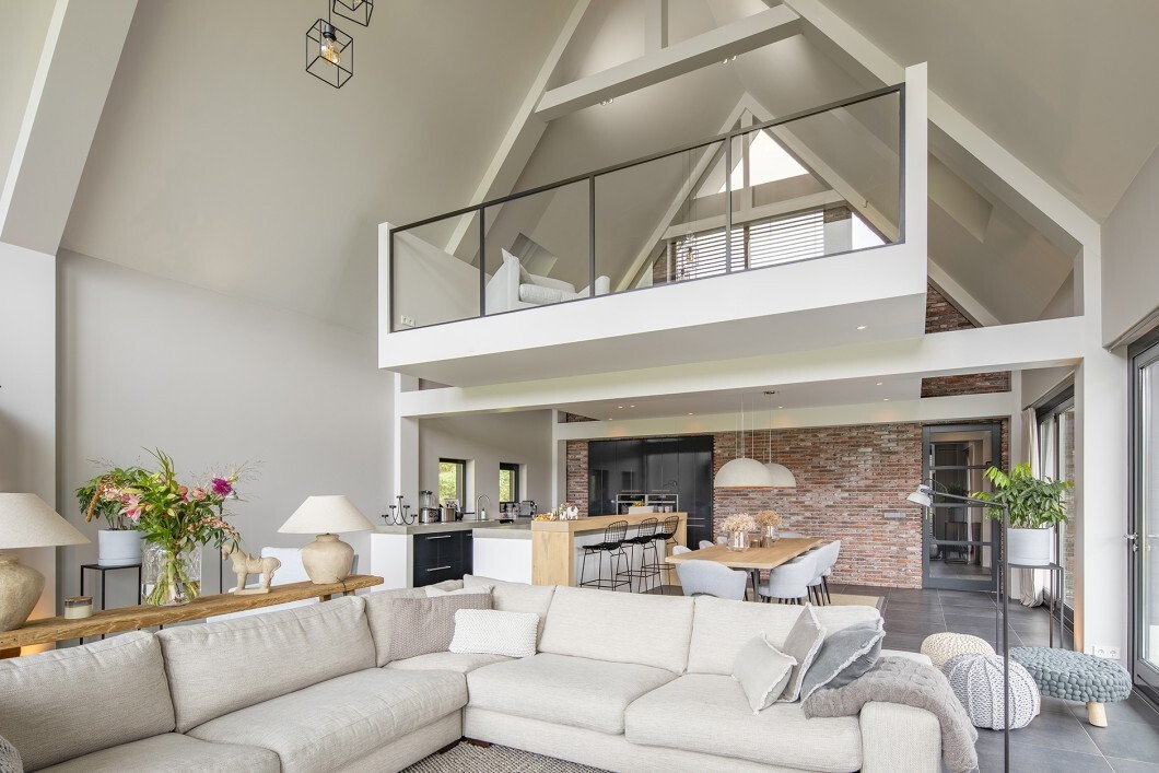 Großzügiges offenes Wohnzimmer mit Loftgalerie, Glasgeländer, Kücheninsel, Esstisch und Sofa.