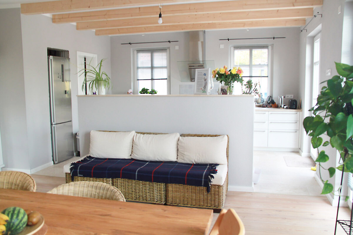 Offener Küchen-Wohnbereich mit Sofa, Pflanzen, Holzdecke und großen Fenstern.
