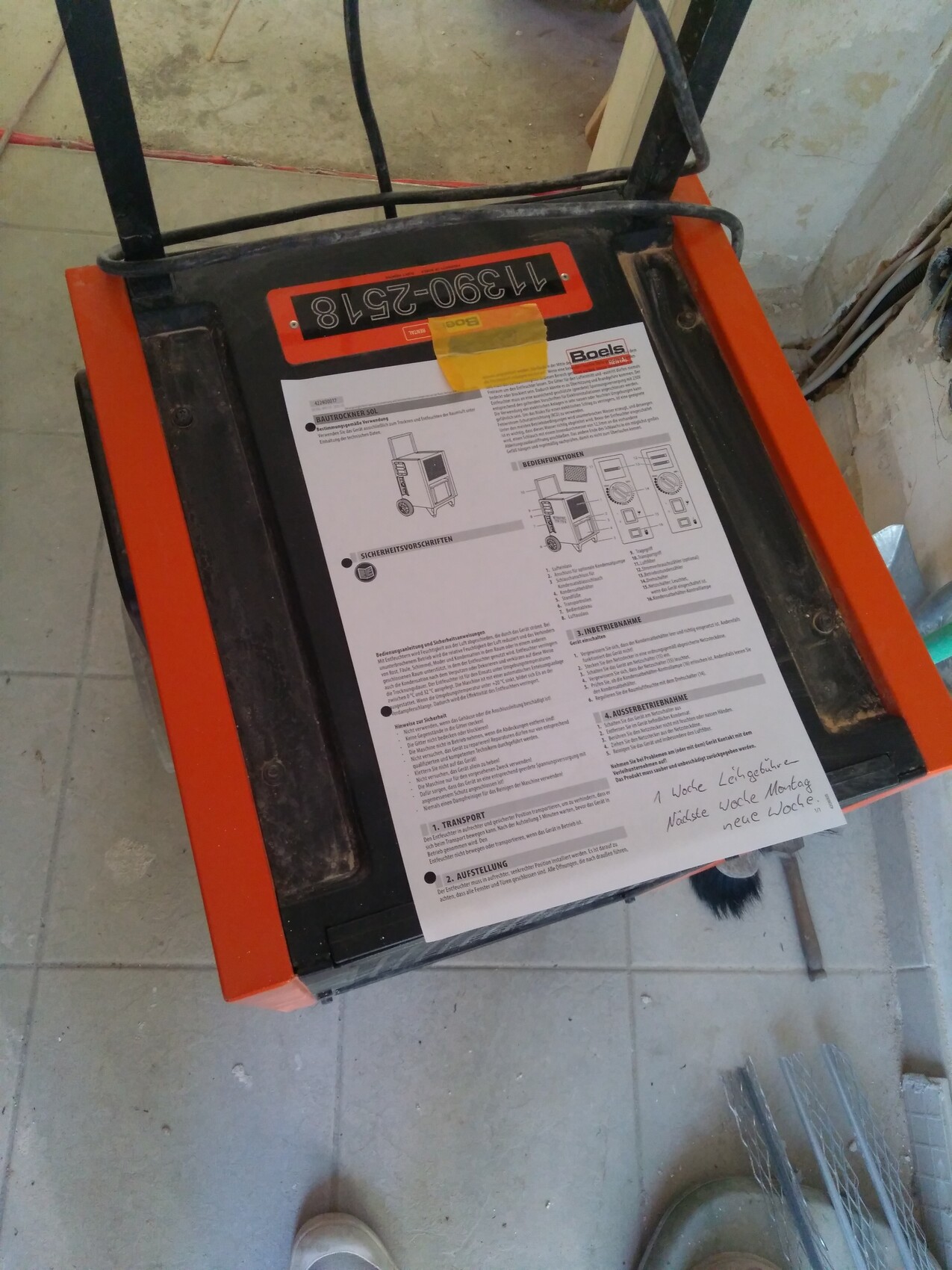 Ein orange gerahmter Bautrockner mit Anleitungspapier liegt auf dem Baustellenboden.