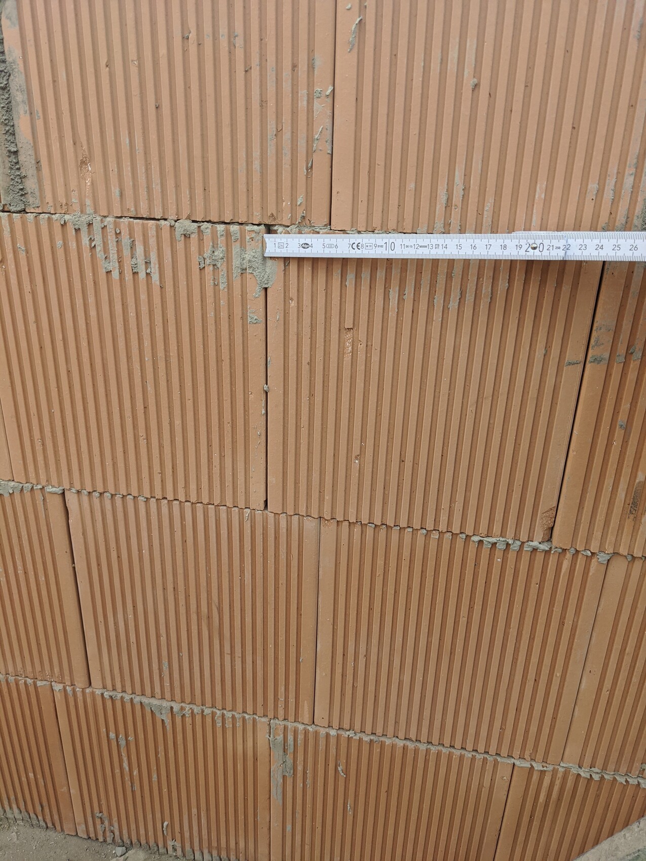 Ziegelwand mit vertikalen Rillen, Mörtelreste und ein waagerecht liegendes Maßband.