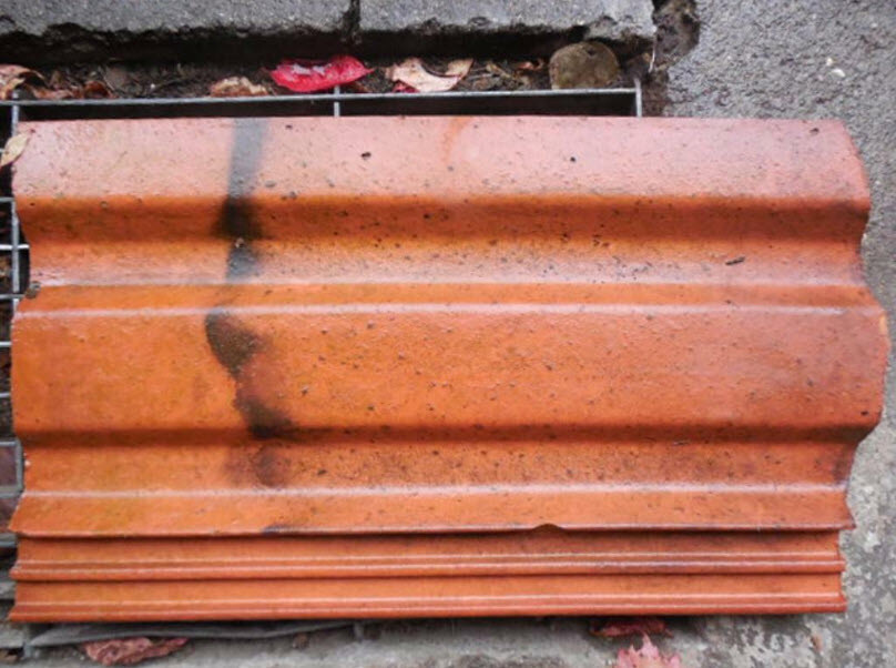 Orangeroter, welliger Dachziegel liegt flach auf dem Boden, verschmutzt.