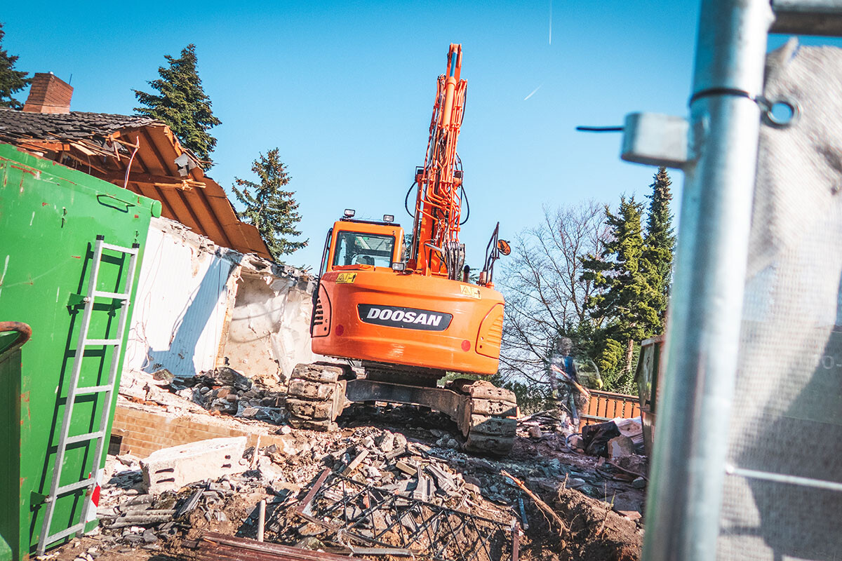 Doosan-Abbruchbagger auf Bauschutt, Bauarbeiter im Hintergrund.
