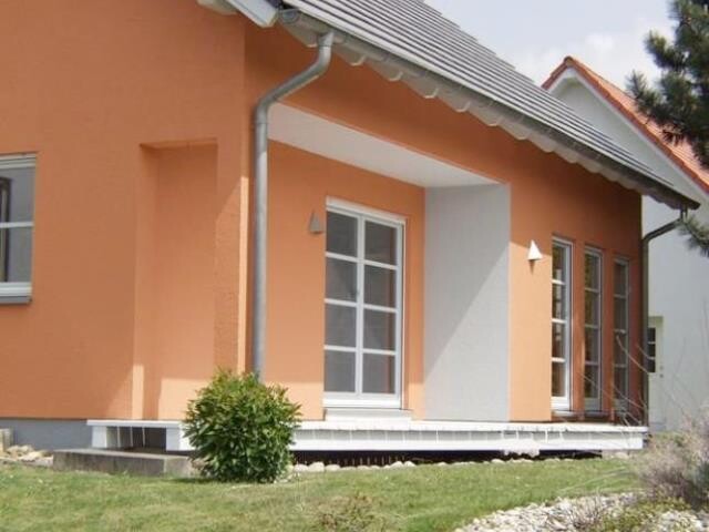 Außenansicht eines orangefarbenen Hauses mit Glas-Tür, Fensterfront und Garten.