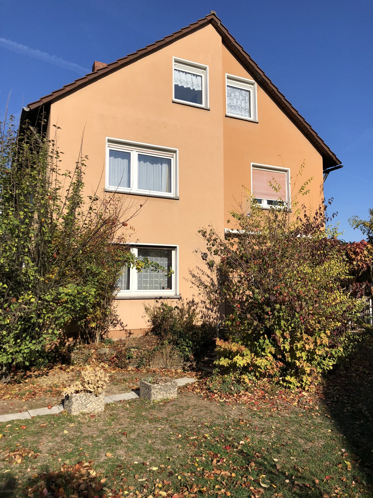 Orangefarbenes, dreistöckiges Haus mit Satteldach; Garten und Herbstlaub davor.