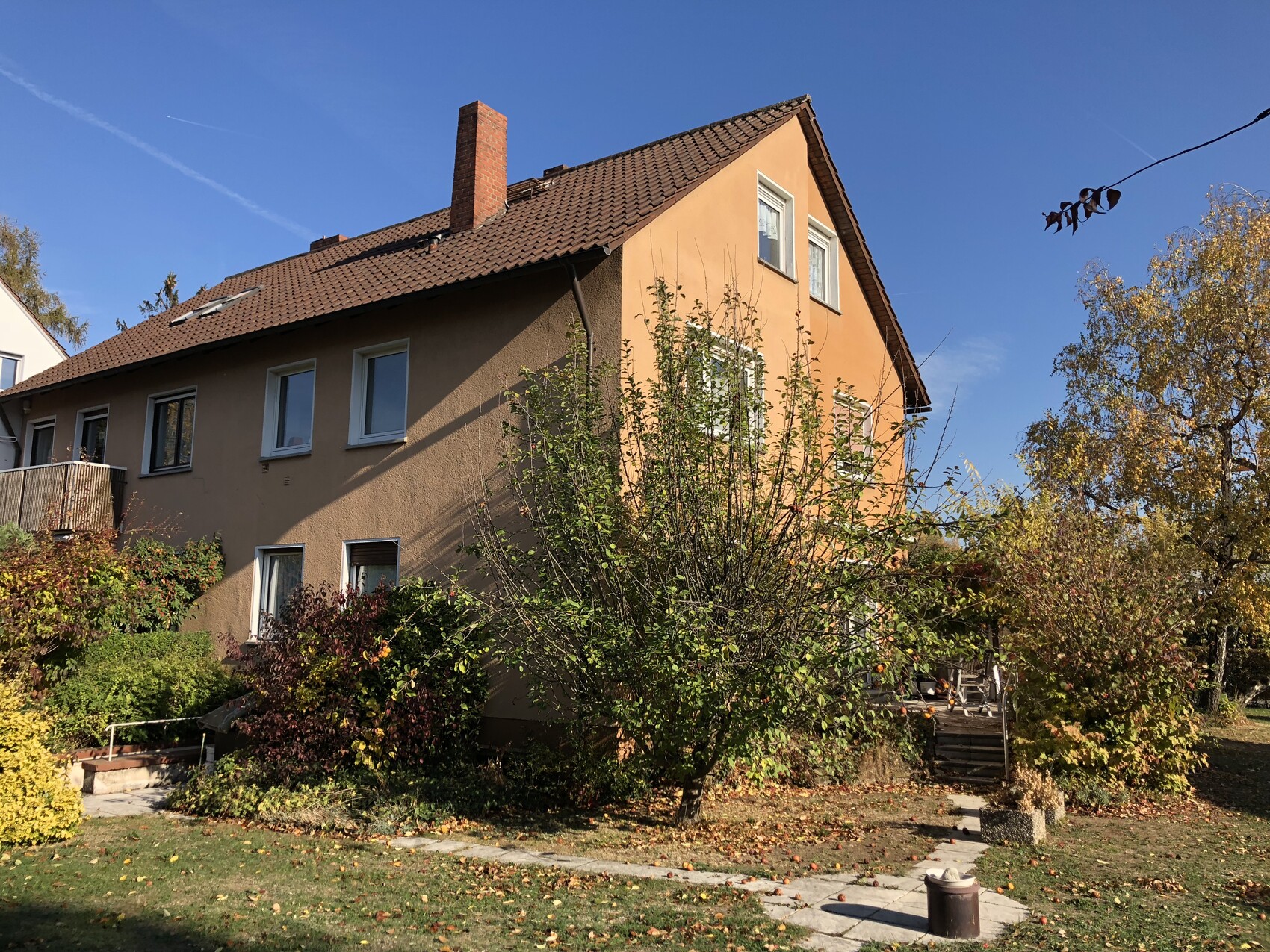 Zweistöckiges Haus mit Fassade in Orange, rotem Dach, Garten mit Herbstlaub und blauem Himmel.