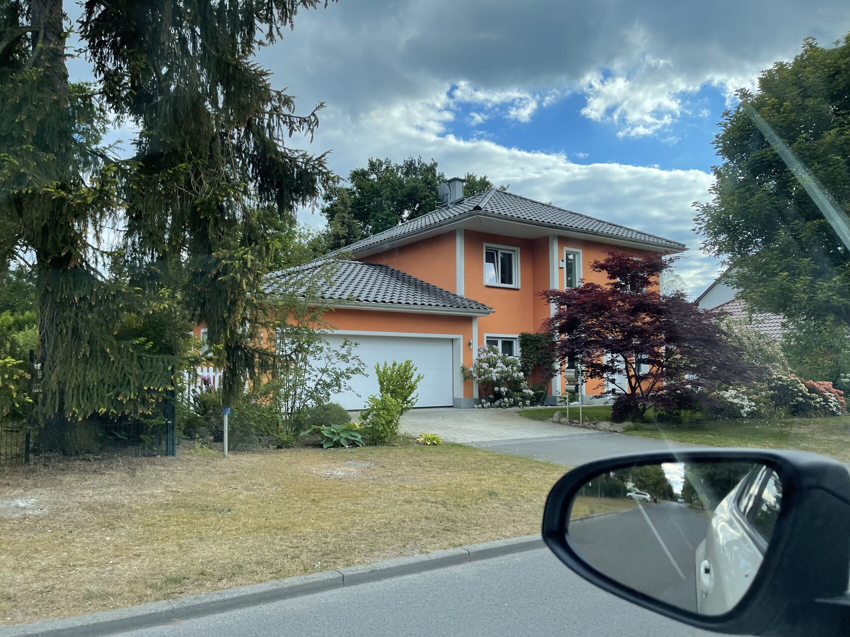 Orangenes zweistöckiges Haus mit Garage, Garten und Bäumen; Autospiegel im Vordergrund.