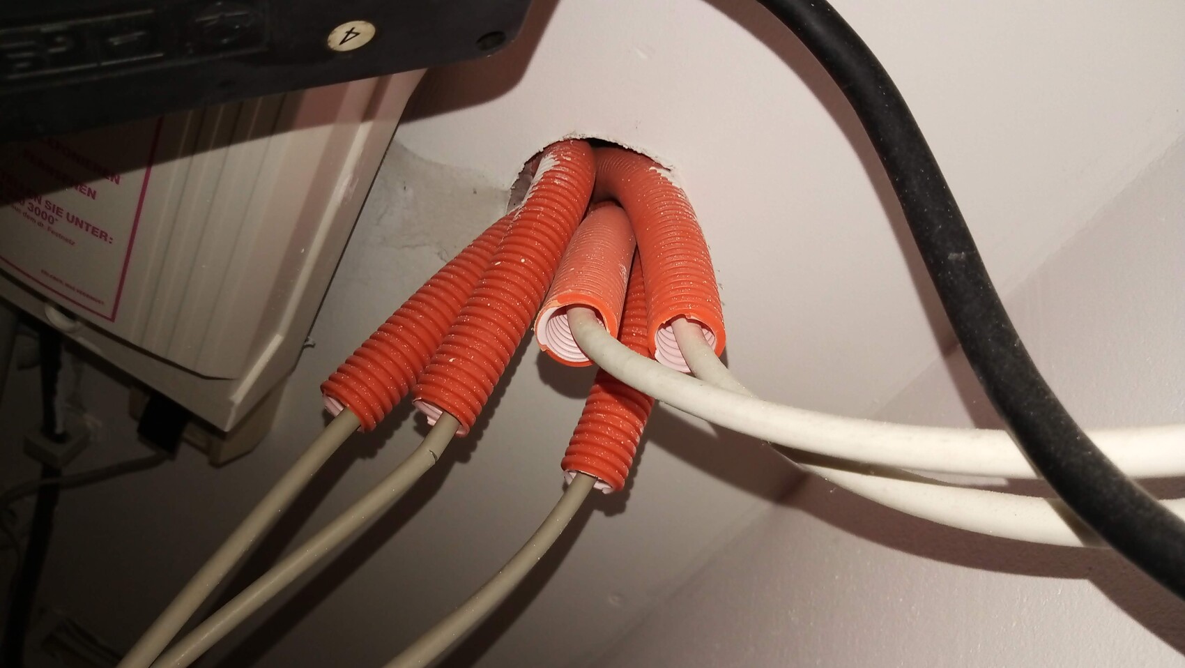 Nahaufnahme: orange Spiralkabelrohre mit weißen Kabeln durch Wanddurchbruch, Elektroinstallation.