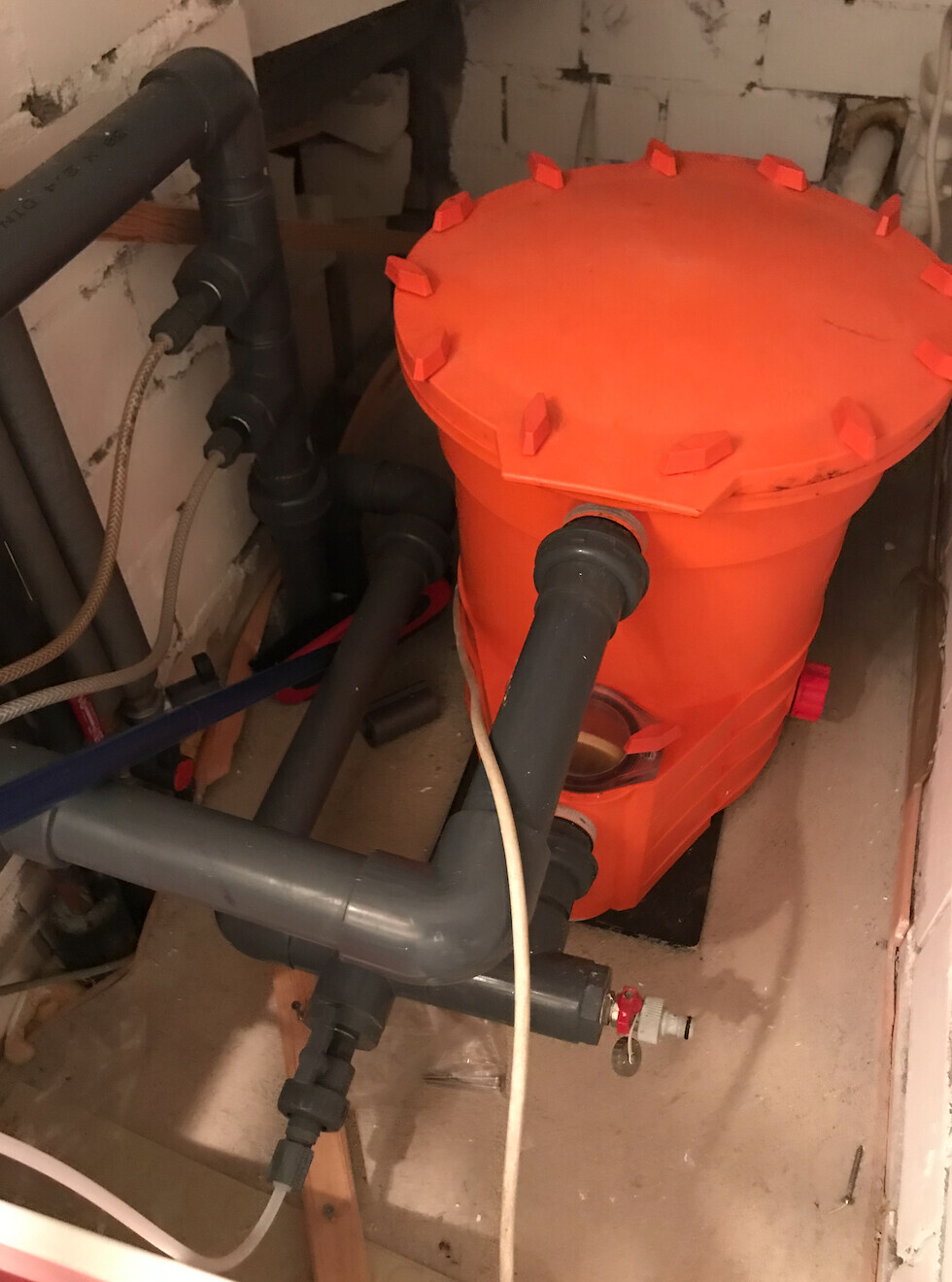 Oranger Filtertank mit Deckel und PVC-Rohren im Installationsraum.