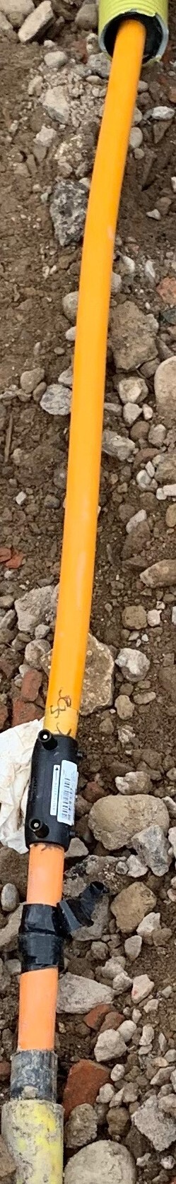 Orangenes Rohr liegt auf Kiesboden, mit schwarzem Anschlussstück und Messmodul.