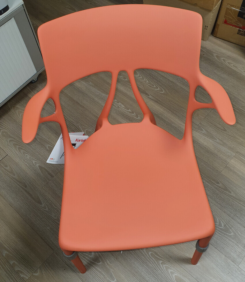 Orangener Kunststoffstuhl mit Armlehnen-Aussparungen auf Holzboden.