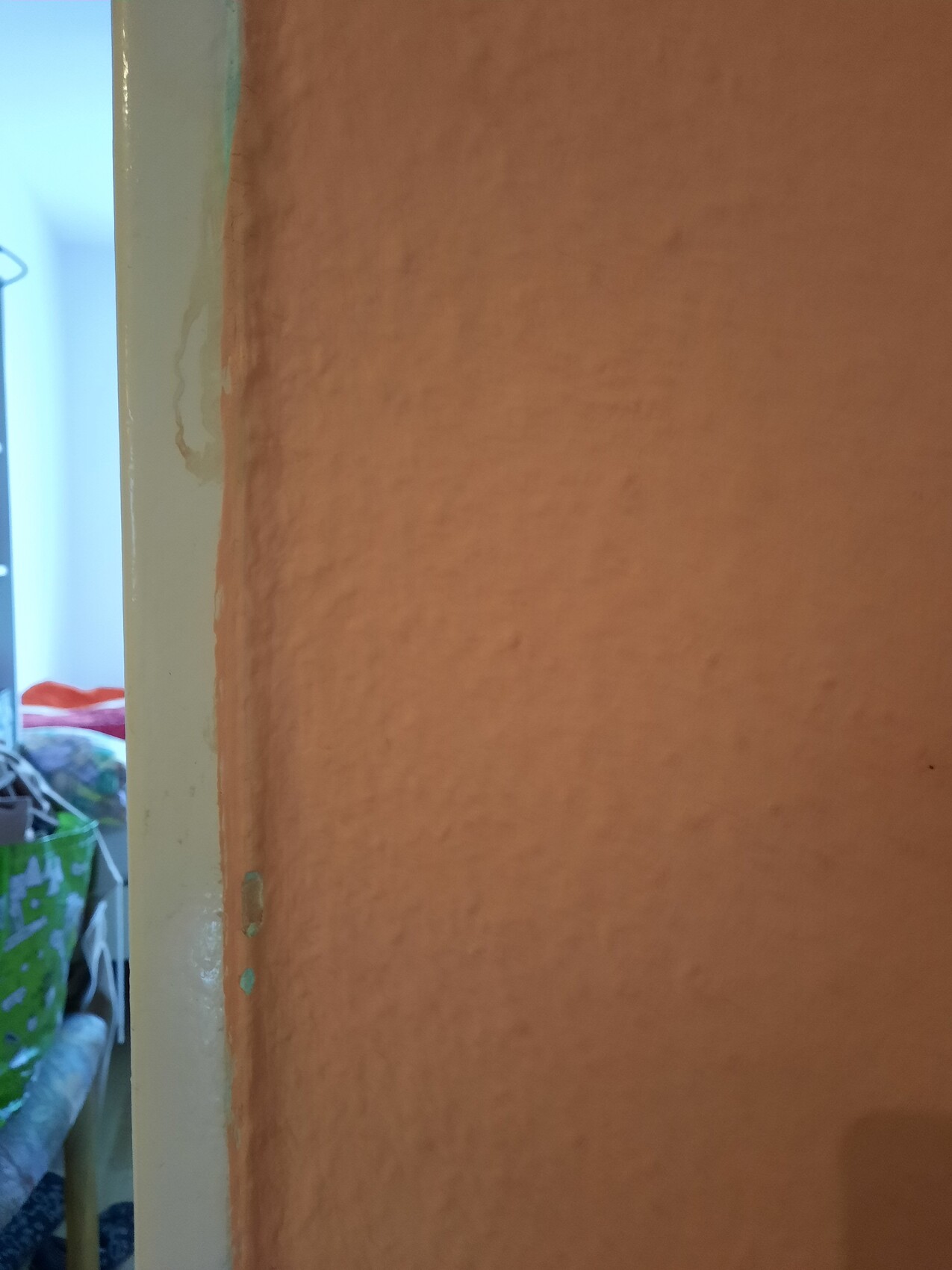 Orange, texturierte Innenwand neben gelblichem Türrahmen; links hindurch sichtbarer Raum mit Wäsche.
