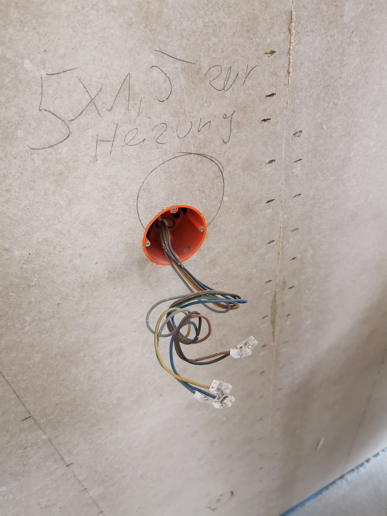 Offene elektrische Kabel aus einer orange Wanddose im Rohbau.