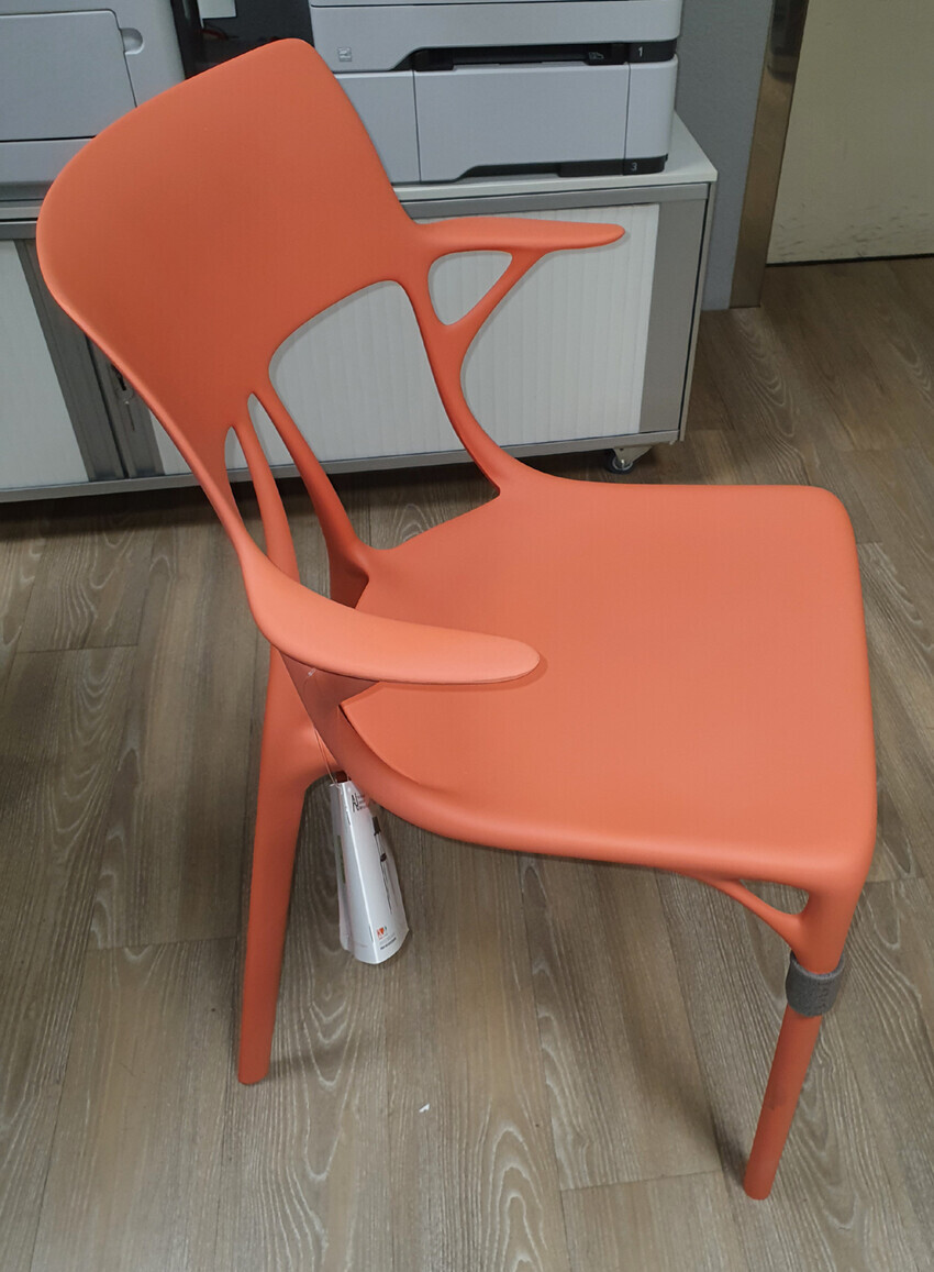Orangener moderner Kunststoffstuhl mit Ausschnitten im Rücken vor einem Kopiergerät im Büro.
