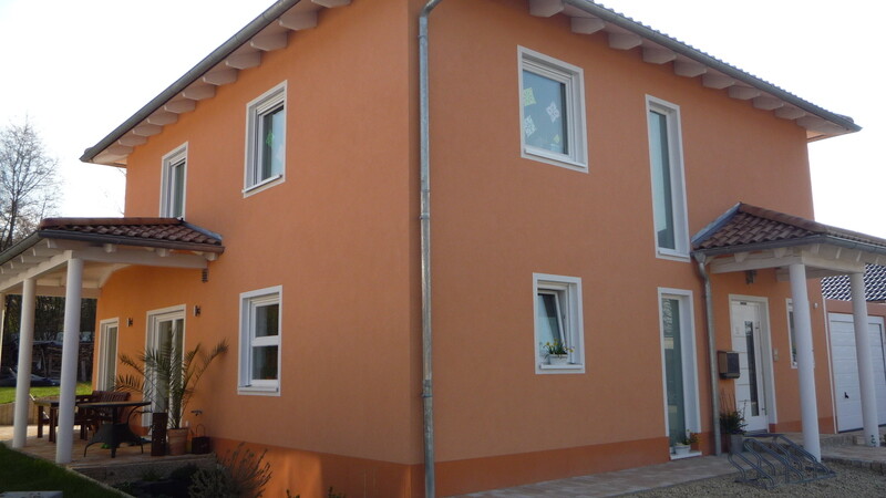 Zweistöckiges orangefarbenes Haus mit weißen Fenstern, Veranda links und Garage rechts.
