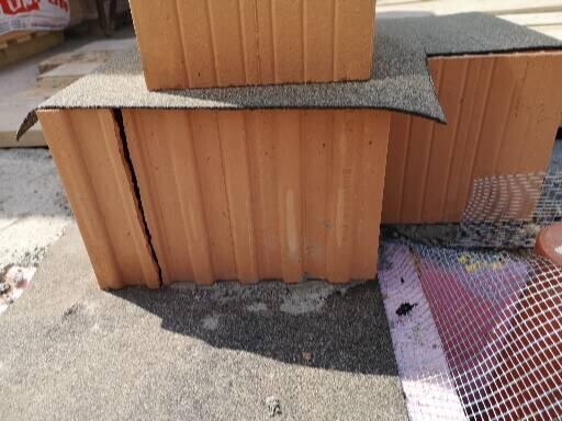 Mehrere braune Kartons stapeln sich auf Asphalt, mit Teppichrest darauf.