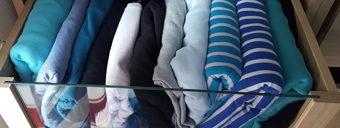 Bunte Kleidung ordentlich gefaltet in einer offenen Schublade eines Kleiderschranks.