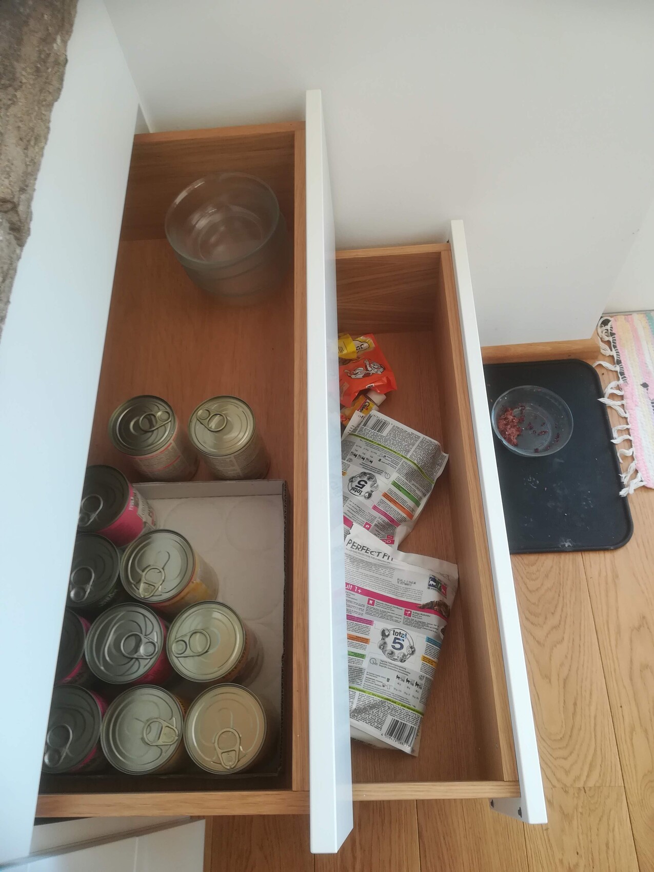 Offene Küchenschublade mit Konservendosen, Snackverpackungen und Zeitungspapierresten.